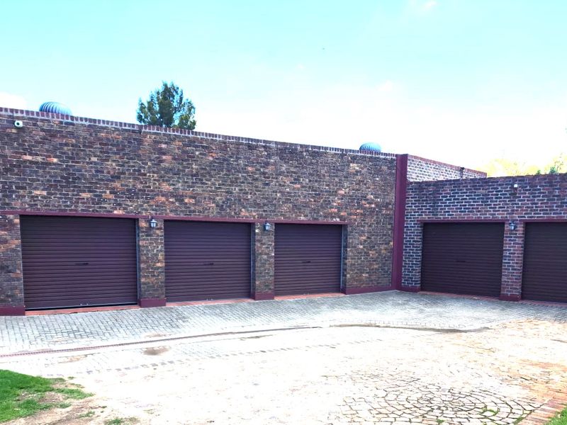 A spacious five-car garage featuring a durable face brick exterior, secure roller shutter doors, and a well-maintained paved driveway.