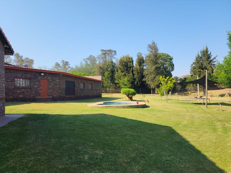 A spacious rear garden featuring a well-maintained lawn, a brick-built swimming pool, and a classic face-brick farmhouse exterior.