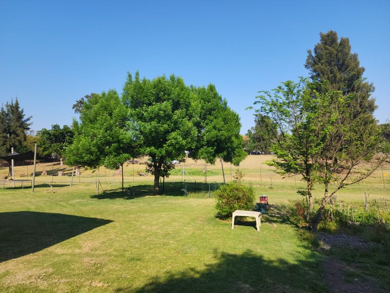 A spacious, well-maintained garden area featuring mature trees and expansive lawn space, typical of a rural farm property setting.