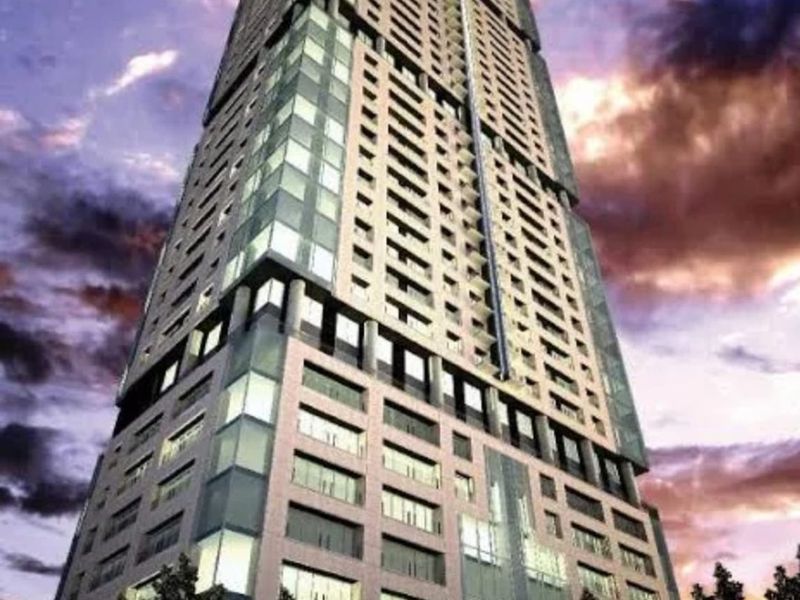 A low-angle view of a modern high-rise apartment building facade featuring glass curtain walls and balconies against a sunset sky.