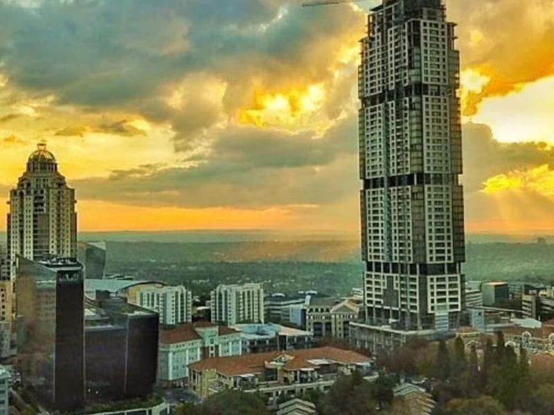 An elevated aerial view of a city skyline featuring high-rise buildings and urban development under a dramatic sunset sky.