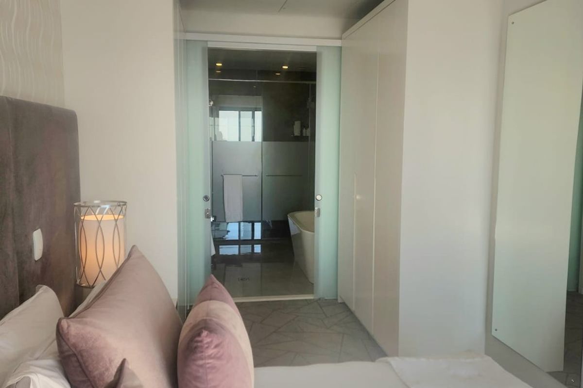 A modern bedroom featuring built-in wardrobes and a sliding glass door leading to an en-suite bathroom with a soaking tub.
