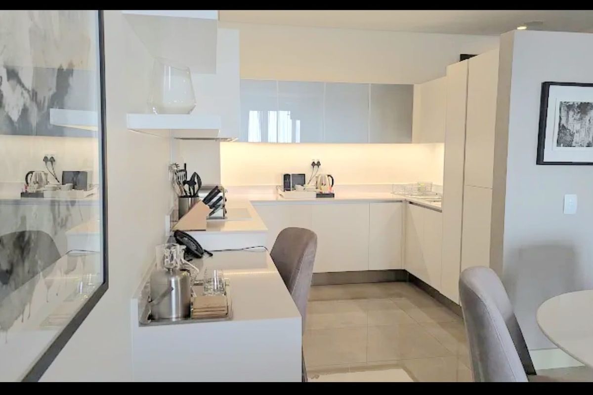 A modern, well-maintained kitchen featuring sleek white cabinetry, stone countertops, and integrated under-cabinet lighting, complemented by neutral tiled flooring.