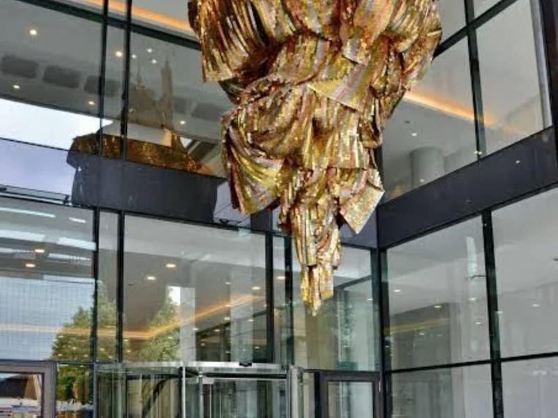 Modern apartment building entrance featuring a full-height glass facade, revolving doors, and a prominent decorative hanging sculpture in the lobby area.