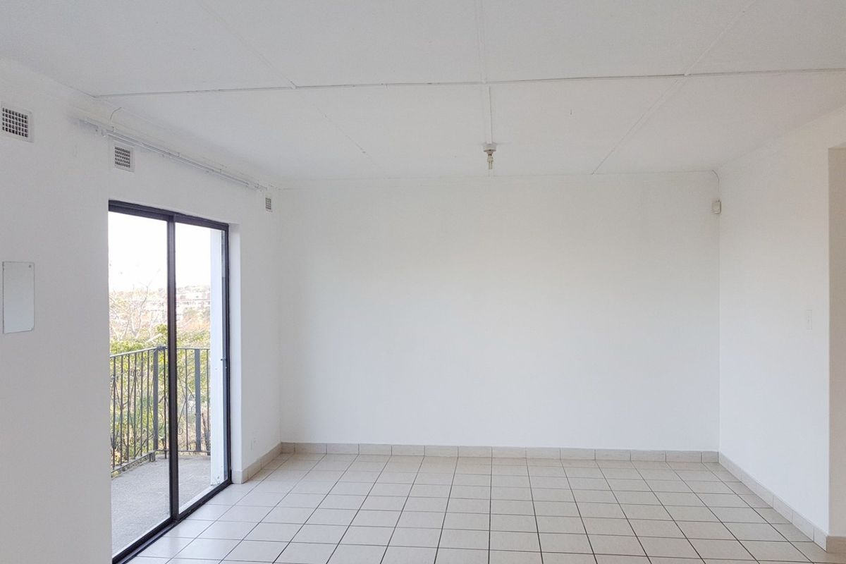A bright, empty living room featuring neutral tiled flooring and a sliding glass door that opens onto a private balcony.