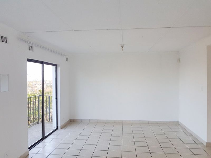 A bright, empty living room featuring neutral tiled flooring and a sliding glass door that opens onto a private balcony.
