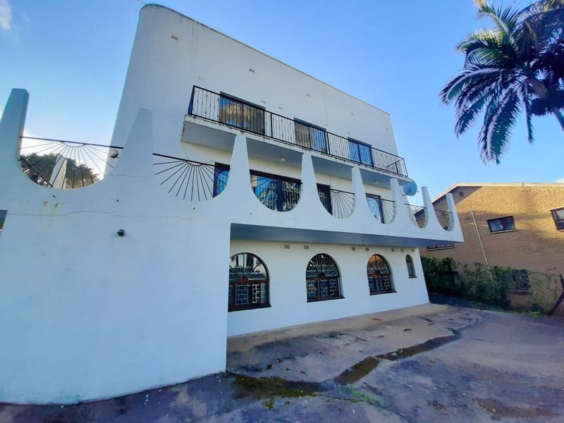 Front elevation of an apartment building featuring distinctive decorative concrete arches, wrought iron balcony railings, and arched windows.