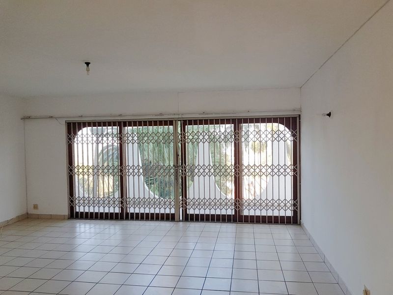 An empty living room featuring tiled flooring and large sliding glass doors secured with a metal security gate.