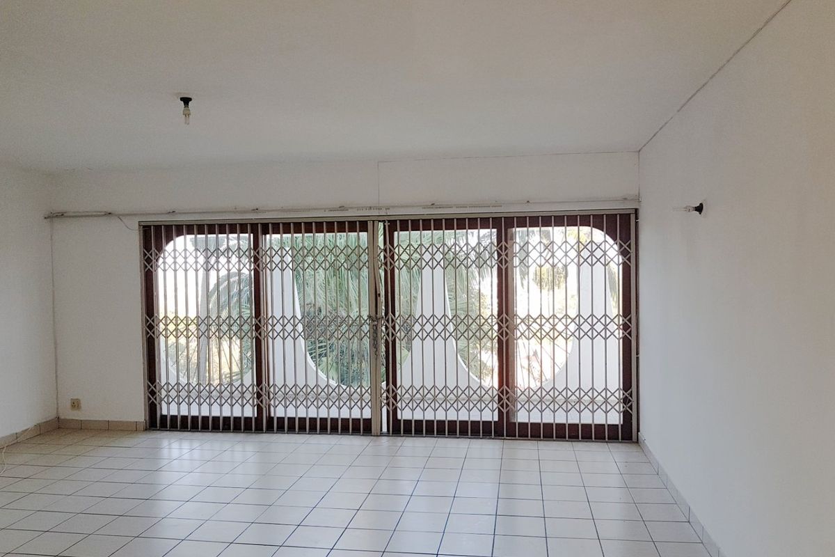 An empty living room featuring white tiled flooring and large sliding glass doors secured with a metal security gate.