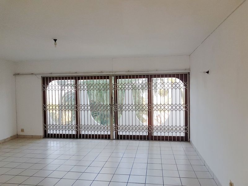 An empty living room featuring white tiled flooring and large sliding glass doors secured with a metal security gate.
