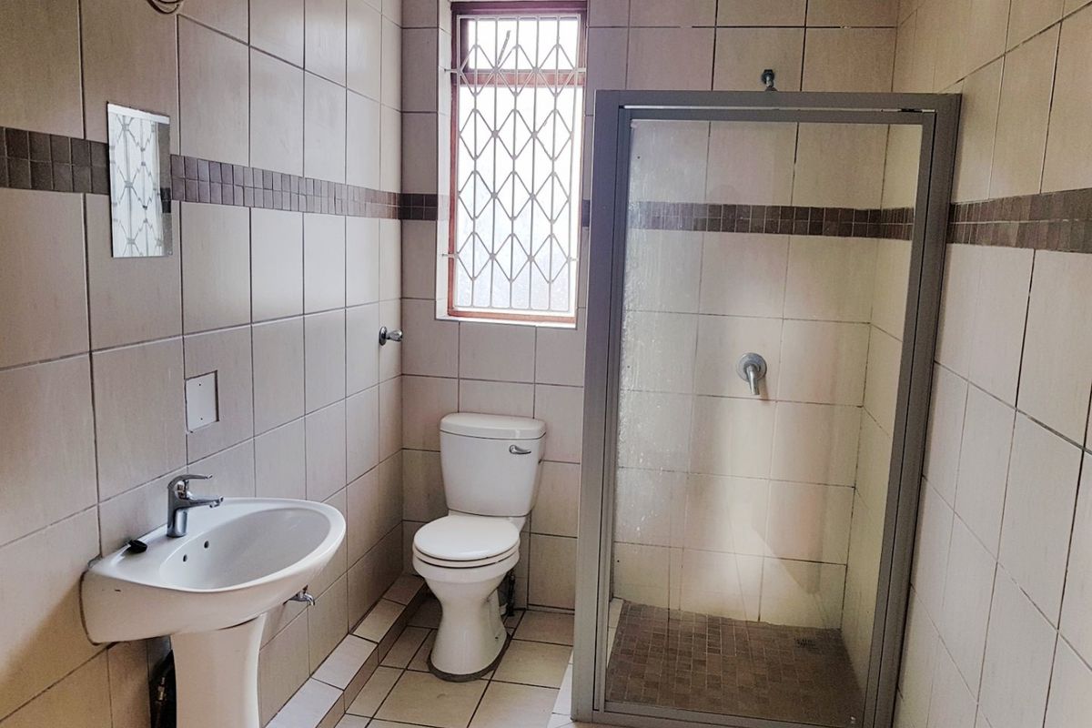 A functional bathroom featuring a pedestal basin, toilet, and a glass-enclosed shower with neutral wall and floor tiling.