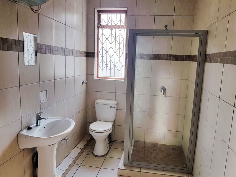 A functional bathroom featuring a pedestal basin, toilet, and a glass-enclosed shower with neutral wall and floor tiling.