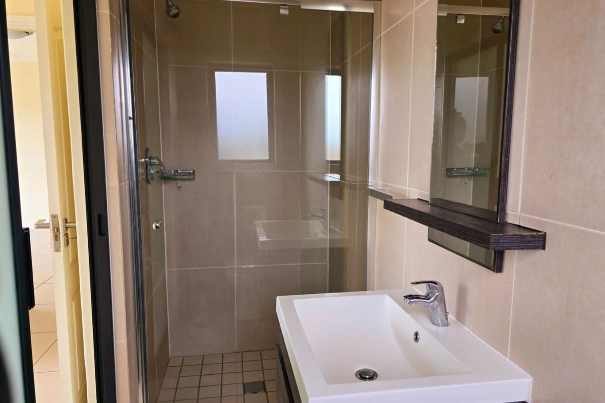 A clean, modern bathroom featuring a glass-enclosed shower, a vanity basin with a mixer tap, and neutral wall tiling.