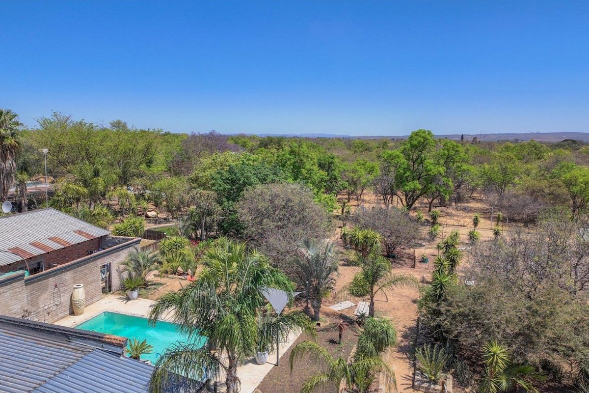 Aerial view of the property grounds featuring a swimming pool, paved patio, and extensive surrounding garden landscape with mature trees.