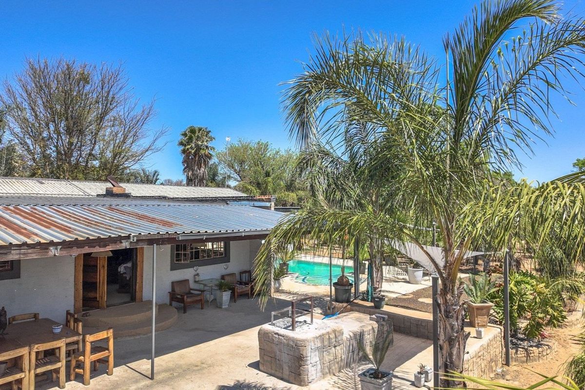 Rear exterior view of the farm property featuring a covered patio, built-in braai area, and a swimming pool set within a landscaped garden.