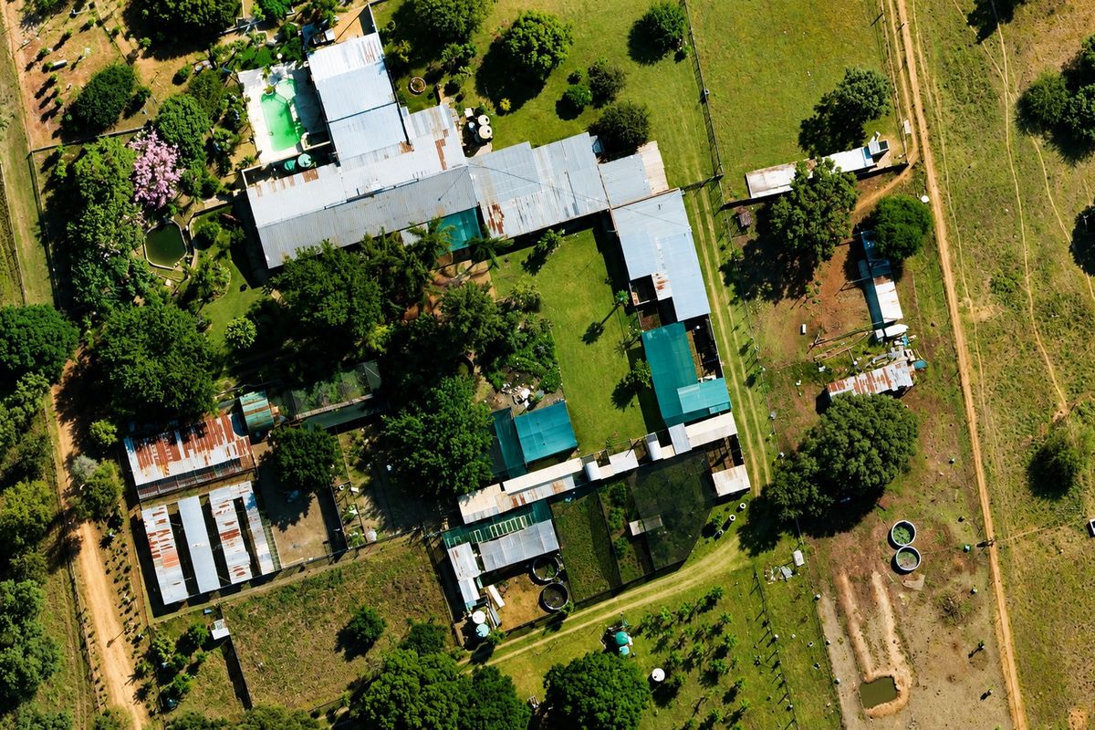 Aerial view of a farm property featuring multiple outbuildings, corrugated metal roofs, a swimming pool, and extensive surrounding land with water storage infrastructure.