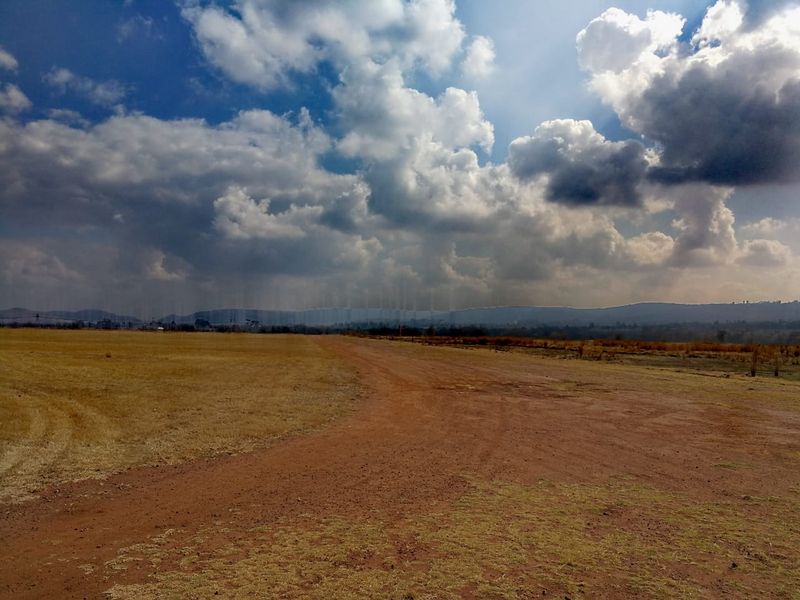 A wide-angle view of an expansive vacant residential plot featuring a dirt access road and open landscape under a cloudy sky.