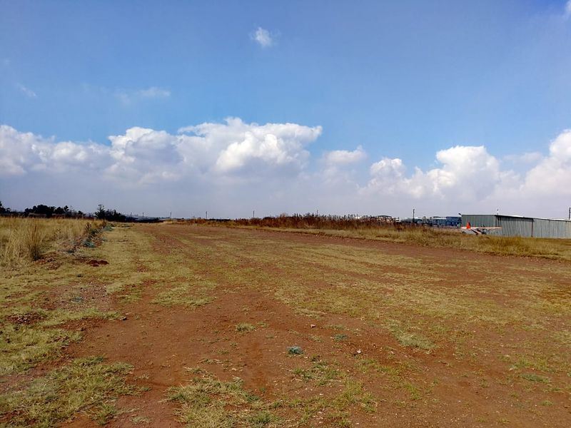 A wide, open expanse of undeveloped residential land featuring natural grass and soil terrain under a clear blue sky.