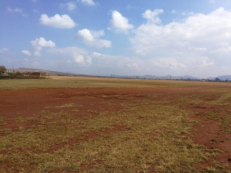A wide-angle view of an expansive, undeveloped residential land plot featuring natural terrain and open space under a clear sky.