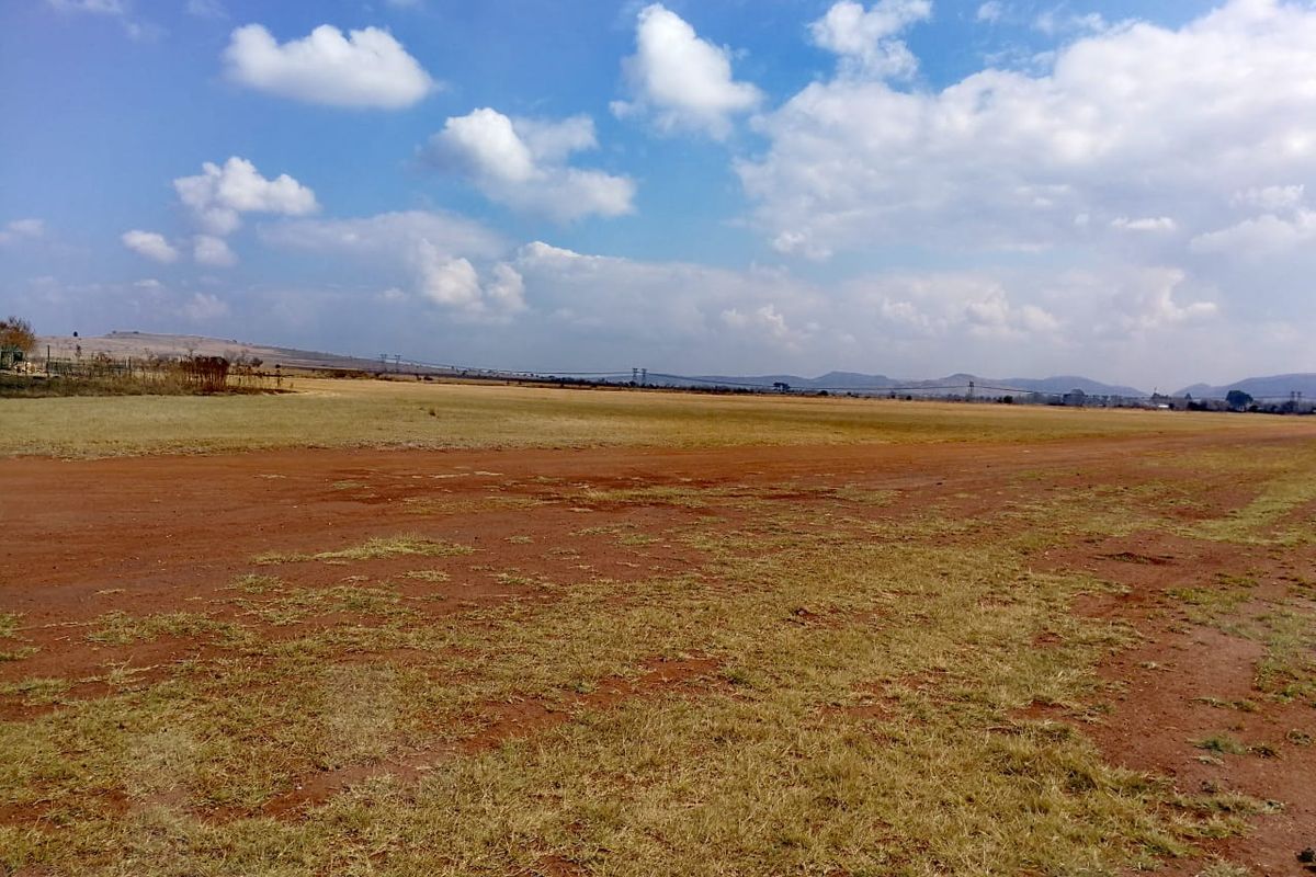 A wide-angle view of a vacant residential plot featuring open, undeveloped land with natural grass and soil under a clear sky.