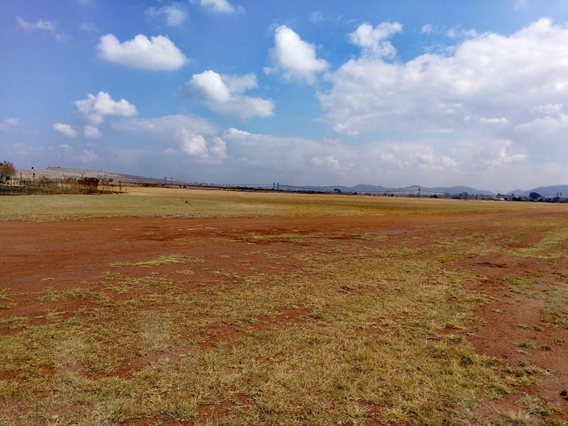 A wide-angle view of a vacant residential plot featuring open, undeveloped land with natural grass and soil under a clear sky.
