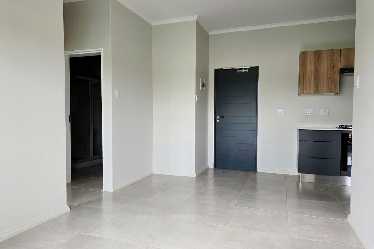A bright, open-plan living and kitchen area featuring neutral tiled flooring, modern cabinetry, and clean finishes, ready for personalization.