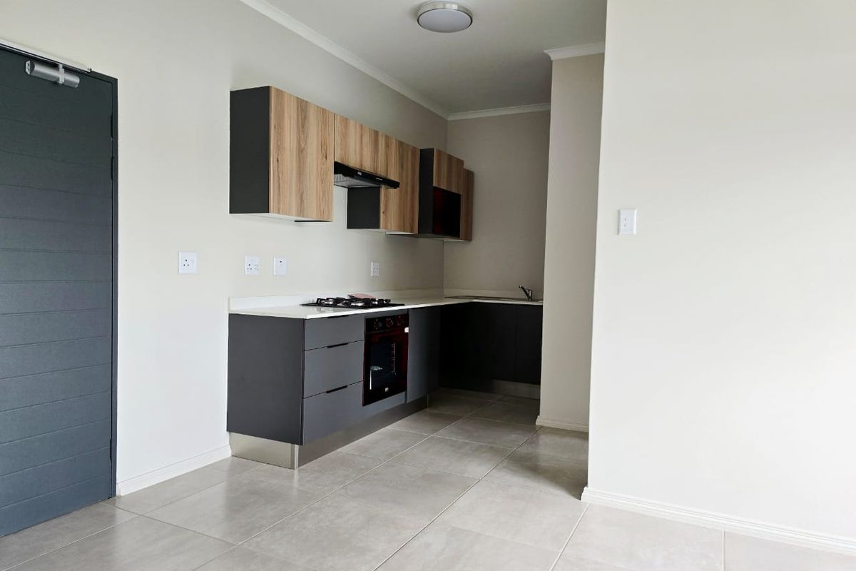 Modern kitchen featuring sleek two-tone cabinetry, integrated hob and oven, extractor fan, and neutral tiled flooring in an open-plan layout.