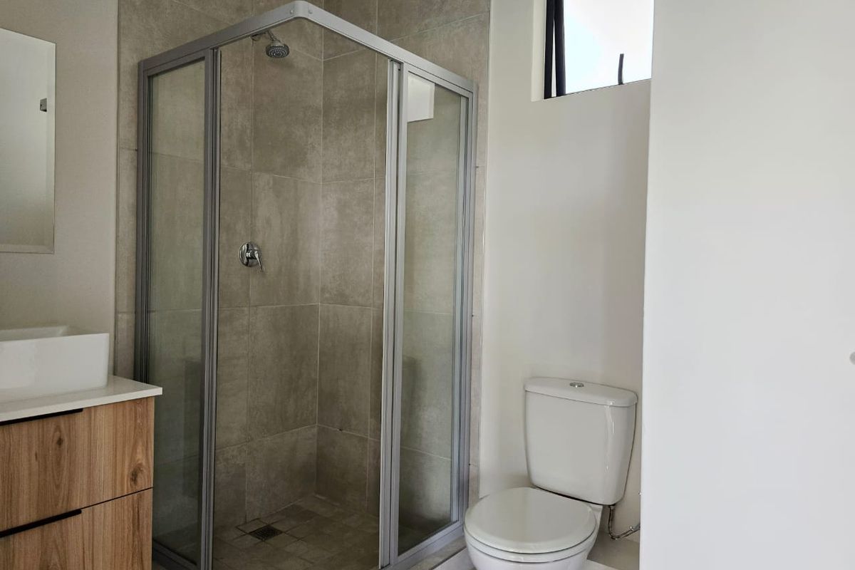 Modern bathroom featuring a glass-enclosed shower, a contemporary vessel sink with a wood-finish vanity cabinet, and a standard toilet.