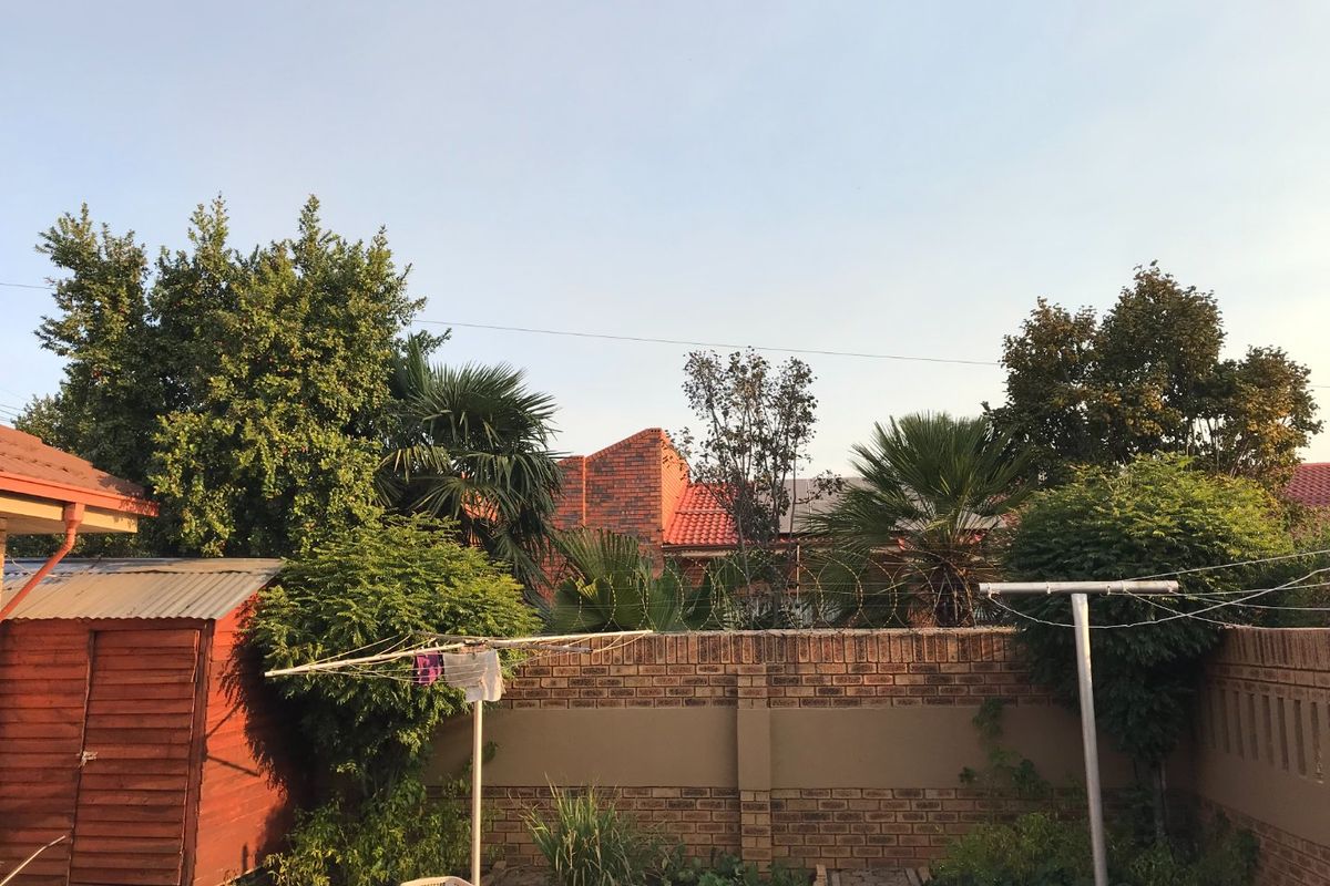 A private rear garden area featuring a brick boundary wall with security fencing, mature trees, and a small wooden storage shed.