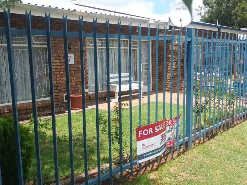 Front view of a face brick townhouse featuring security fencing, security bars on windows, and a satellite dish.