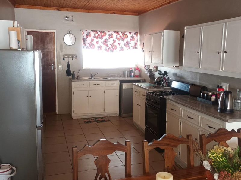 A functional kitchen featuring timber ceilings, tiled flooring, built-in cabinetry, and a freestanding stove, offering a practical layout with potential for modern updates.