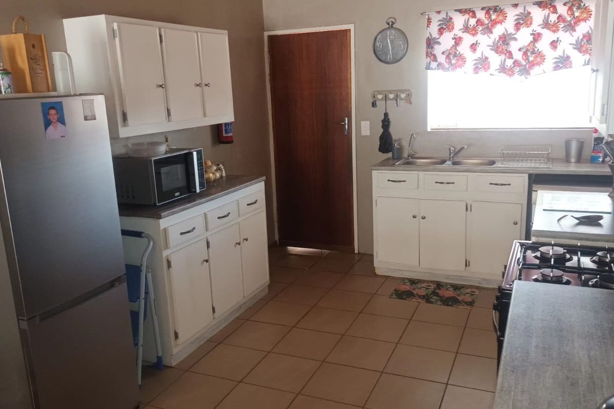 A functional kitchen featuring white built-in cabinetry, laminate countertops, a double basin sink, and a gas hob with tiled flooring.