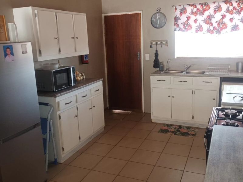 A functional kitchen featuring white built-in cabinetry, laminate countertops, a double basin sink, and a gas hob with tiled flooring.