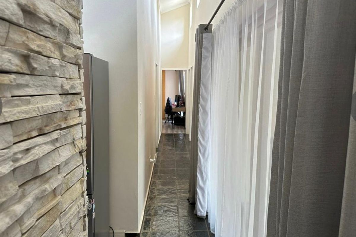 A long hallway featuring dark tiled flooring, a textured stone cladding feature wall, and a high vaulted ceiling with recessed lighting.