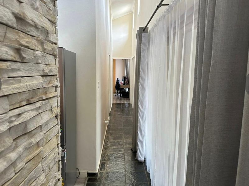 A long hallway featuring dark tiled flooring, a textured stone cladding feature wall, and a high vaulted ceiling with recessed lighting.