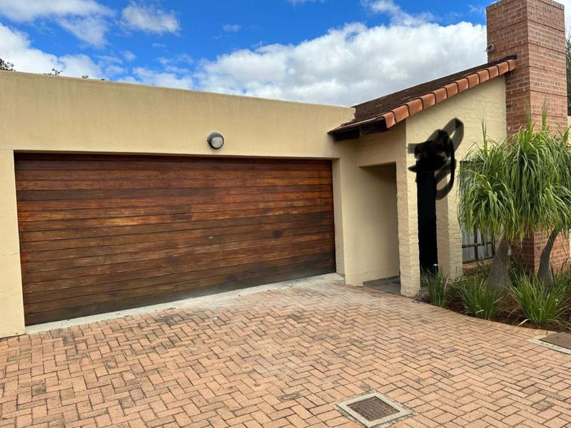 Front exterior view of a townhouse featuring a timber garage door, brick chimney, and paved driveway.