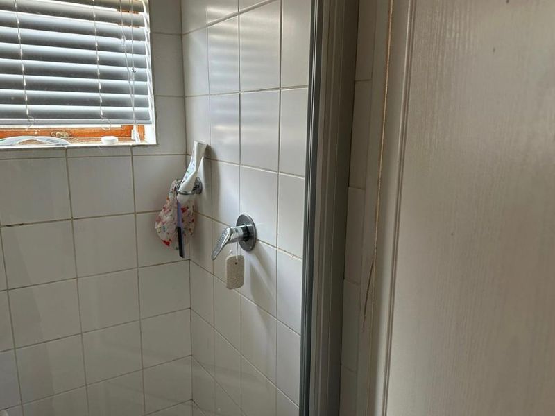 A compact bathroom shower area featuring white wall tiles, a chrome mixer tap, and a window with a venetian blind.