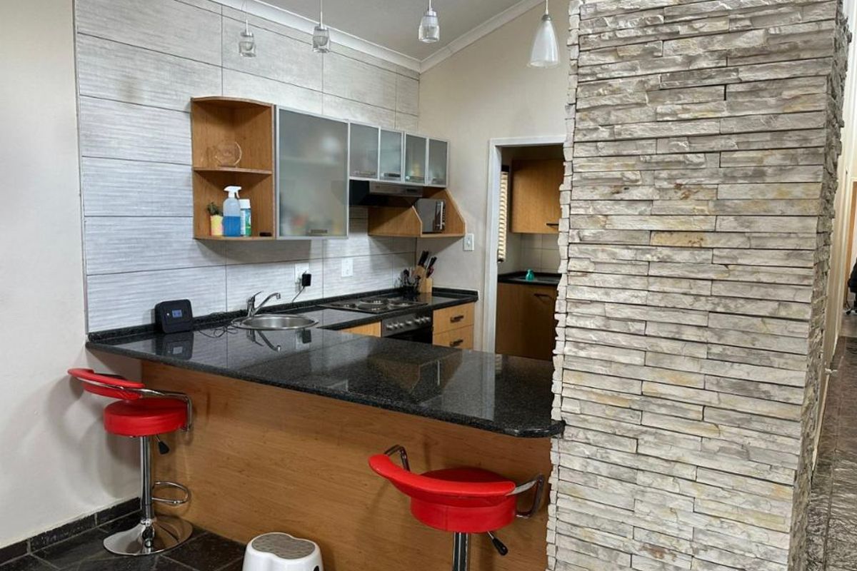 Modern kitchen featuring granite countertops, built-in cabinetry, a stainless steel hob, and a distinctive stone veneer feature wall with breakfast bar seating.