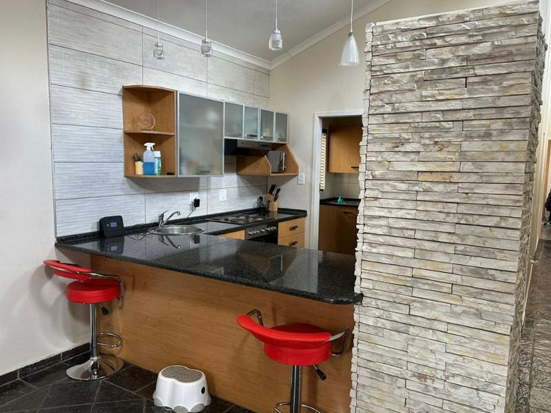 Modern kitchen featuring granite countertops, built-in cabinetry, a stainless steel hob, and a distinctive stone veneer feature wall with breakfast bar seating.