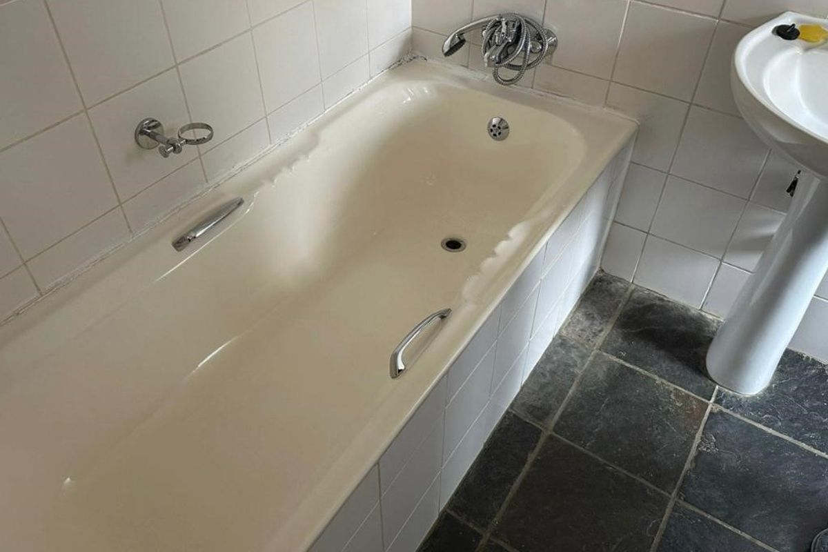 A functional bathroom featuring a bathtub with chrome fixtures, a pedestal basin, and dark stone floor tiles, requiring cosmetic updates to modernize the space.