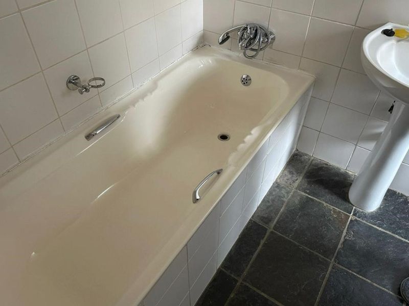 A functional bathroom featuring a bathtub with chrome fixtures, a pedestal basin, and dark stone floor tiles, requiring cosmetic updates to modernize the space.