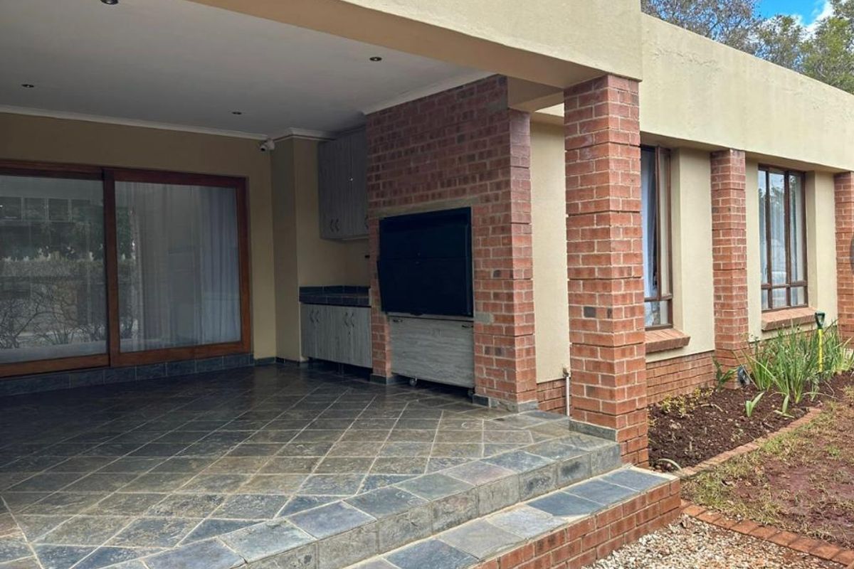 Covered patio area featuring a built-in braai, tiled flooring, and brick pillar accents, providing a functional outdoor entertainment space.