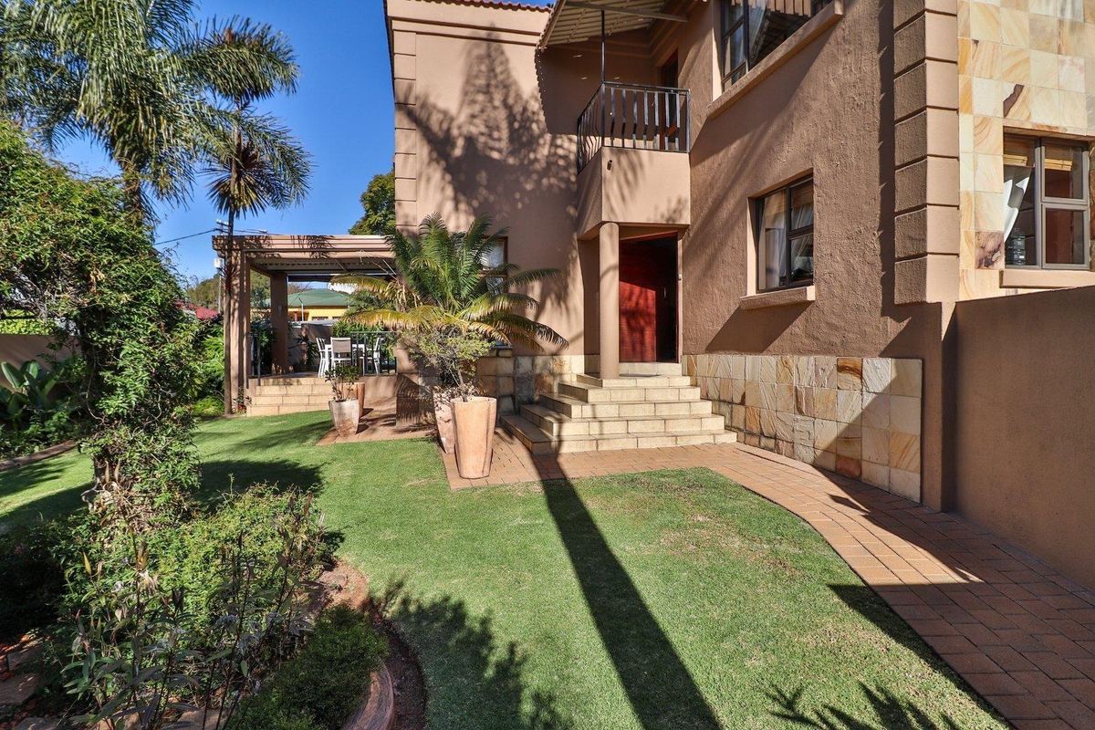 A well-maintained rear exterior view featuring a landscaped garden, paved walkway, stone-clad facade, and a covered patio area.