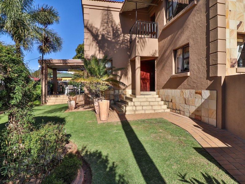 A well-maintained rear exterior view featuring a landscaped garden, paved walkway, stone-clad facade, and a covered patio area.