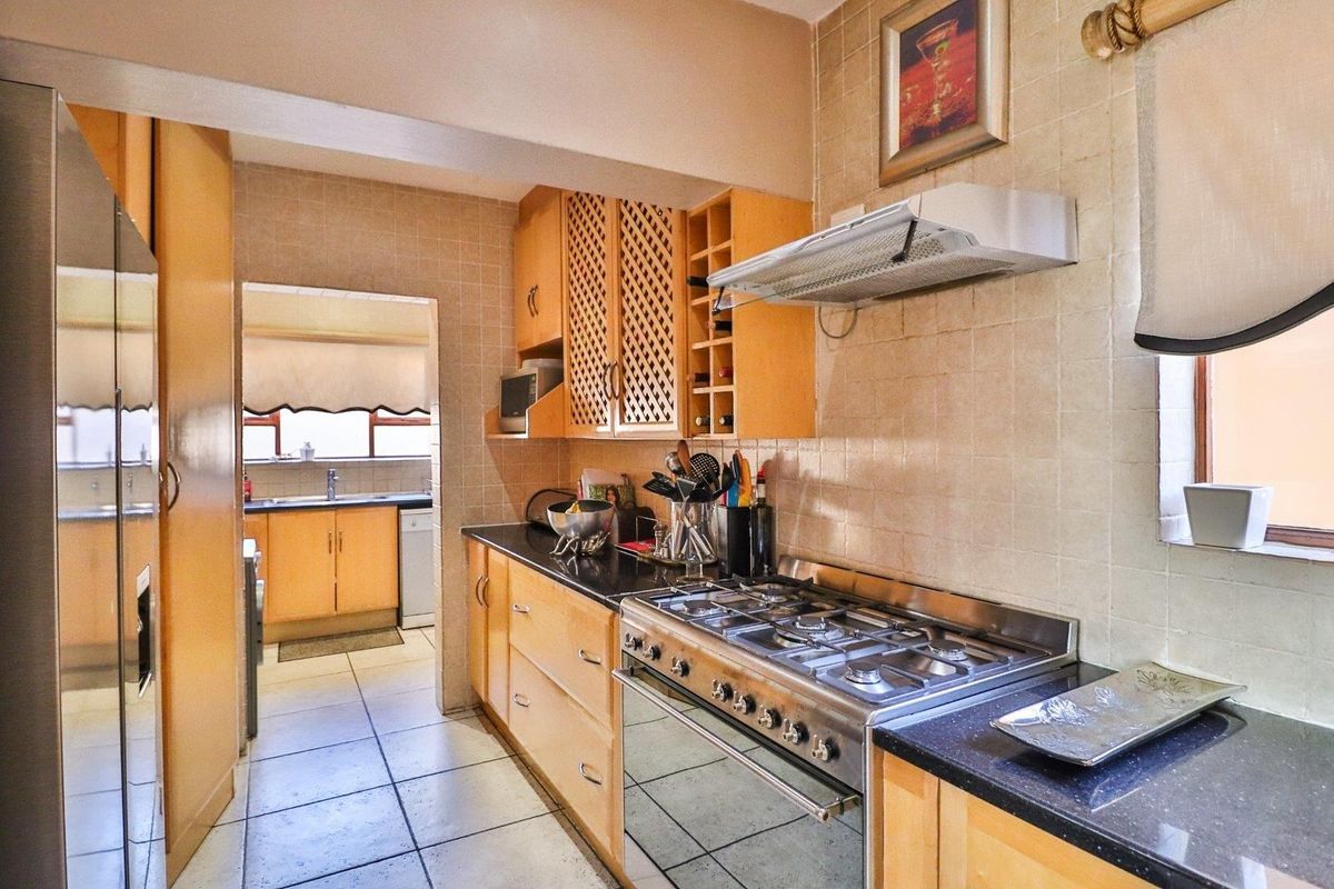 A functional kitchen featuring wooden cabinetry, granite countertops, a gas stove with extractor fan, and tiled finishes throughout.