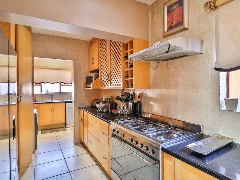 A functional kitchen featuring wooden cabinetry, granite countertops, a gas stove with extractor fan, and tiled finishes throughout.