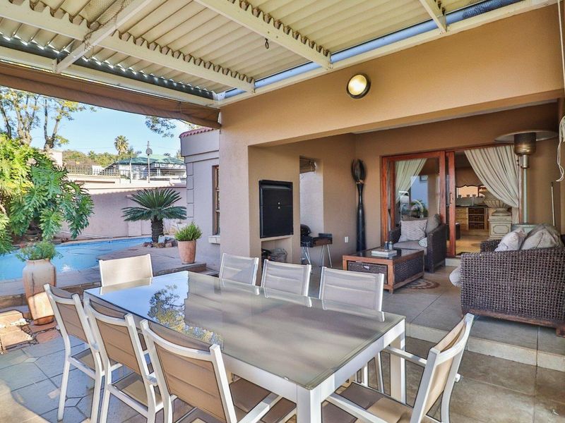 A spacious covered patio featuring tiled flooring, a built-in braai, and direct access to the swimming pool area through sliding glass doors.