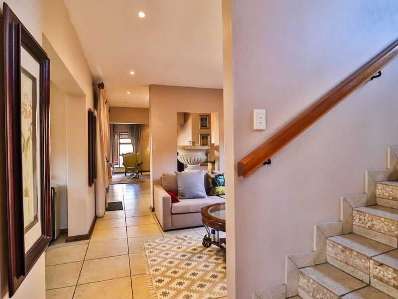A bright hallway featuring tiled flooring and a staircase with a wooden handrail, leading into an open-plan living area.