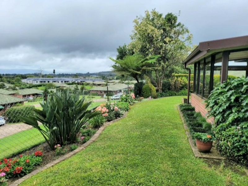 A well-maintained garden area featuring a lush lawn, landscaped flower beds with brick edging, and a view of the surrounding neighborhood.