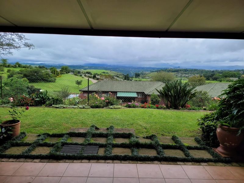 A covered patio overlooking a well-maintained garden with expansive views of the surrounding green landscape.